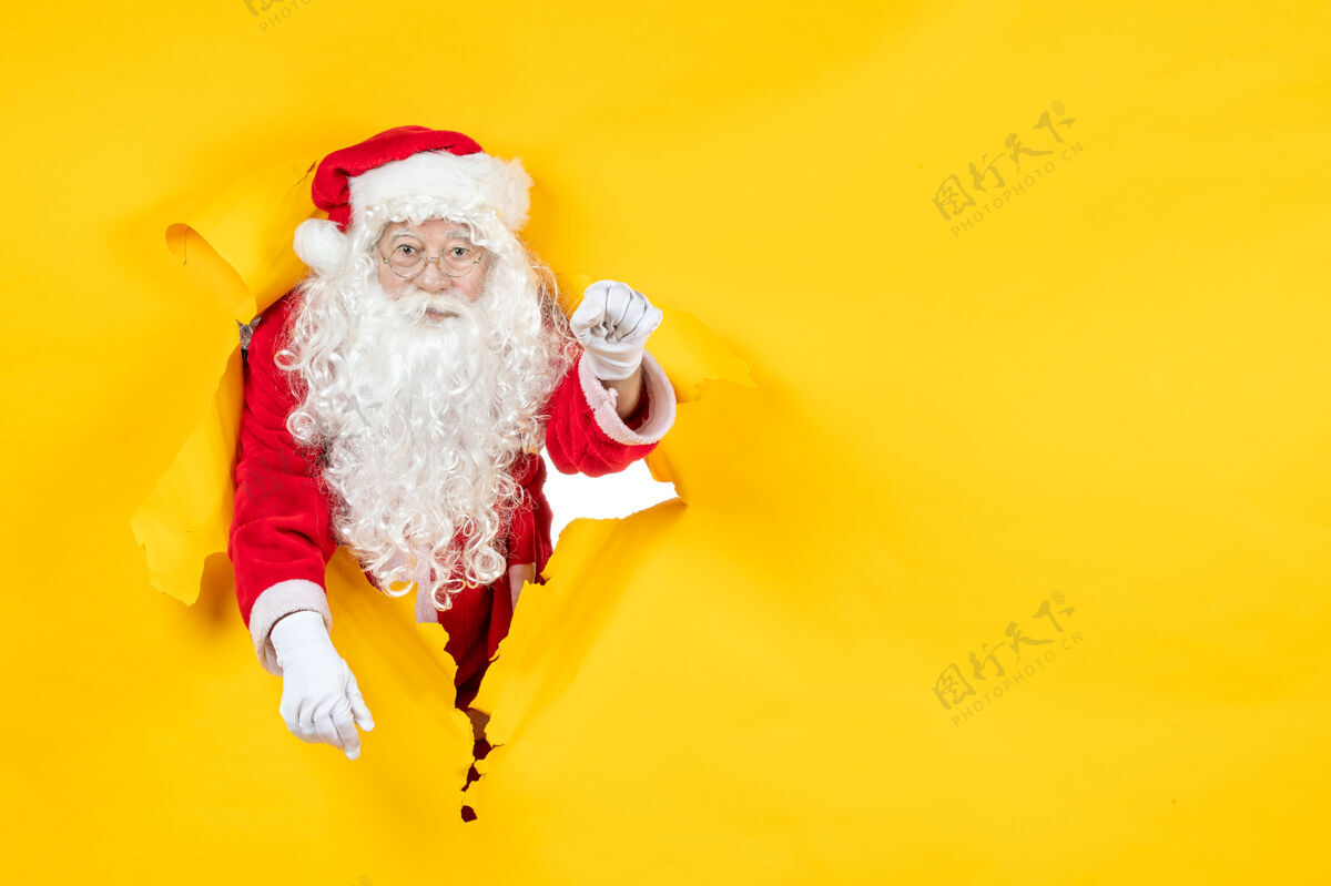 帽子圣诞老人透过撕破的纸黄色墙壁看的正视图十二月纸庆祝