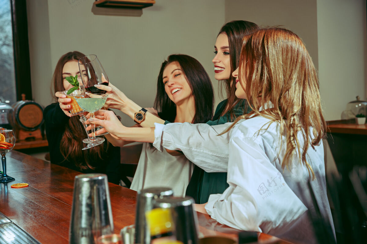 咖啡馆女朋友们在酒吧喝酒 她们坐在一张摆着鸡尾酒的木桌旁 她们在碰杯微笑朋友食物