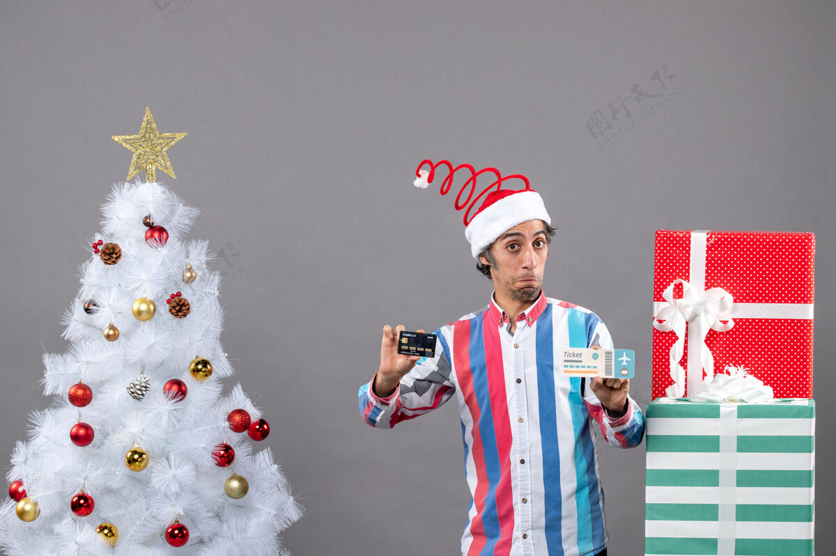 灰色前视图混乱的人拿着卡片和旅行票绕圣诞树和礼物微笑人无辜