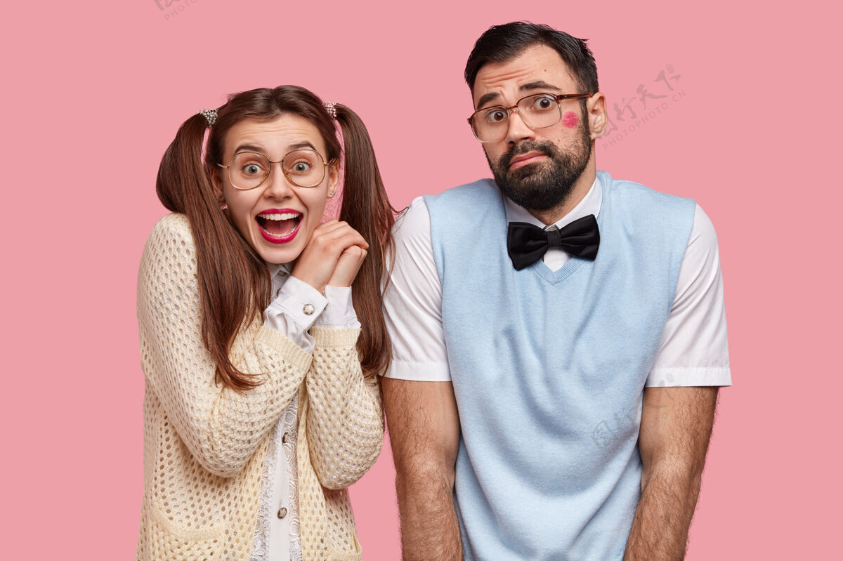 衣服快乐的年轻欧洲女人和男人的水平镜头 带着喜悦和犹豫的表情 有第一次约会 不知道如何表现 穿旧的时髦衣服 隔着粉红色的墙同学优雅室内