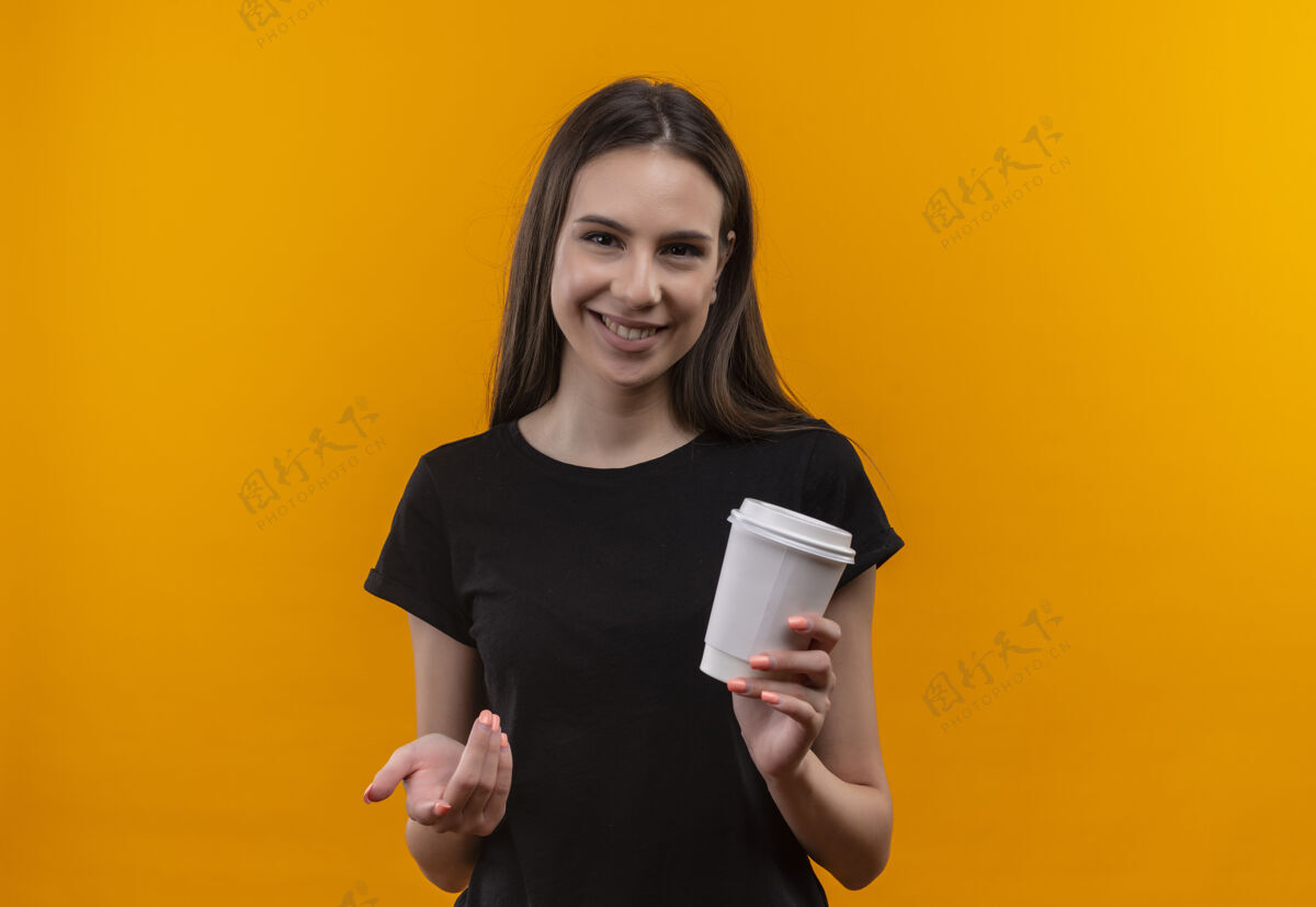 拿着微笑着的年轻白人女孩穿着黑色t恤 手里拿着一杯咖啡 在孤立的橙色背景下对着镜头杯子T恤微笑