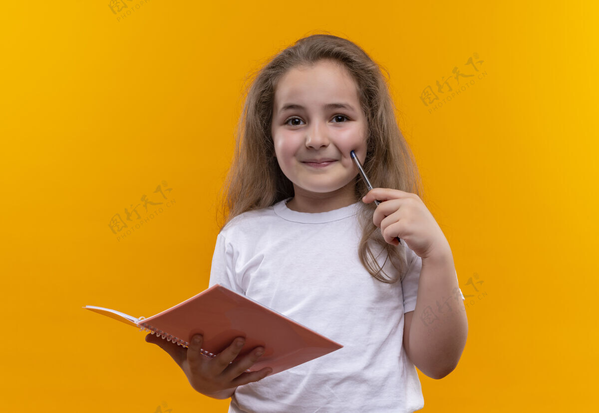 学校微笑的小女孩穿着白色t恤 拿着笔记本和笔 背景是孤立的橙色小微笑拿着