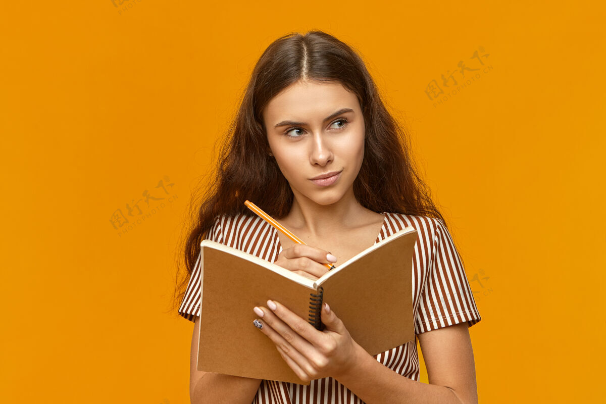 美女美丽的学生女孩穿着条纹连衣裙拿着日记和钢笔家庭作业Copybook大学