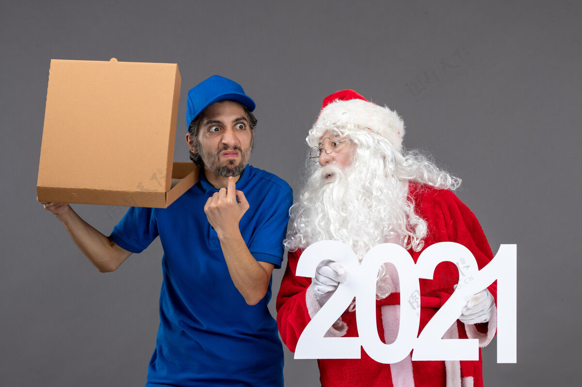 服装圣诞老人的正面图 灰色的墙上有男信使拿着购物袋和食品盒人快乐圣诞老人