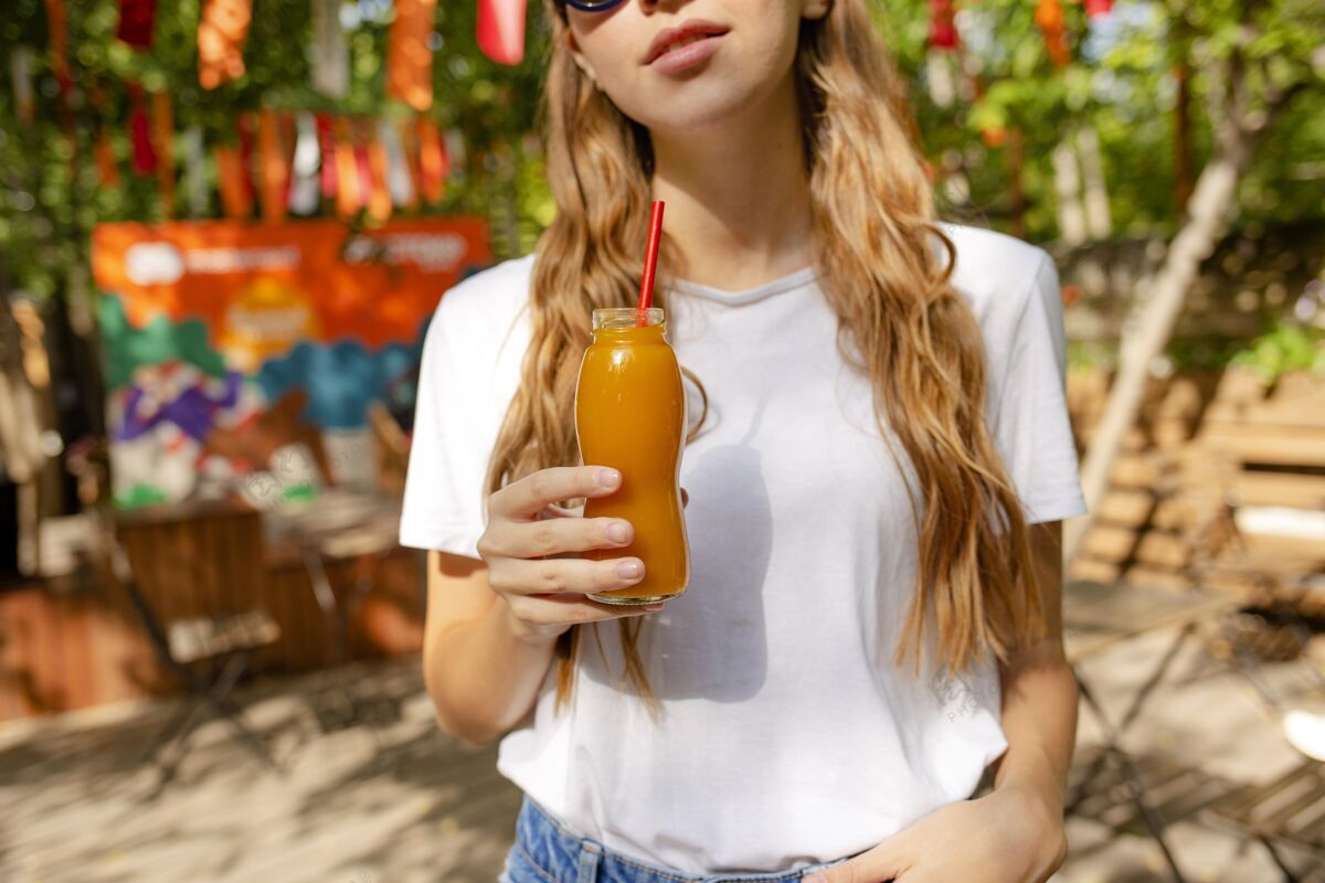 提神中镜头的女孩拿着新鲜的果汁瓶在公园里热带食品健康食品