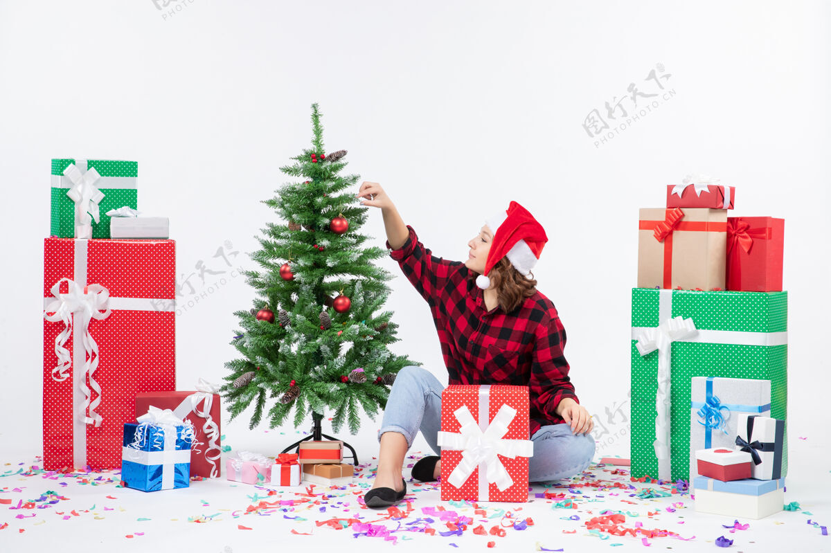 冬青年轻女子围坐在圣诞礼物和白色墙上的小圣诞树前的视图坐礼物礼物