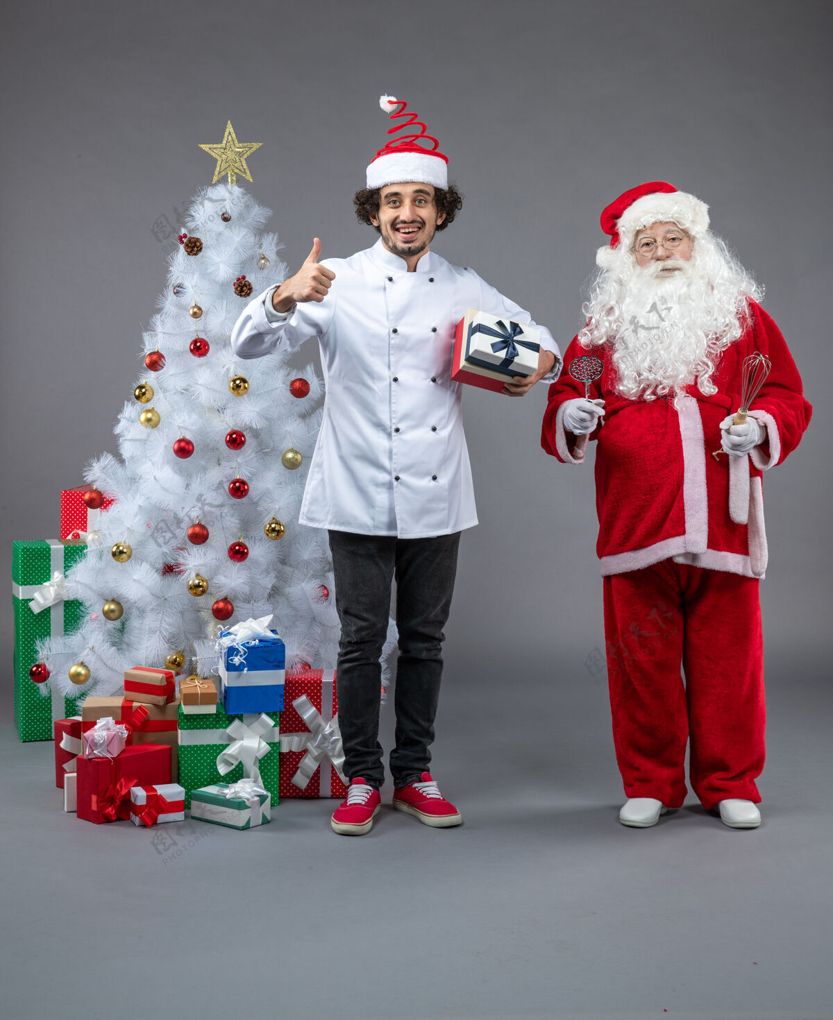 快乐圣诞老人与男性厨师和圣诞礼物在灰色墙壁周围的正面视图厨师圣诞男性