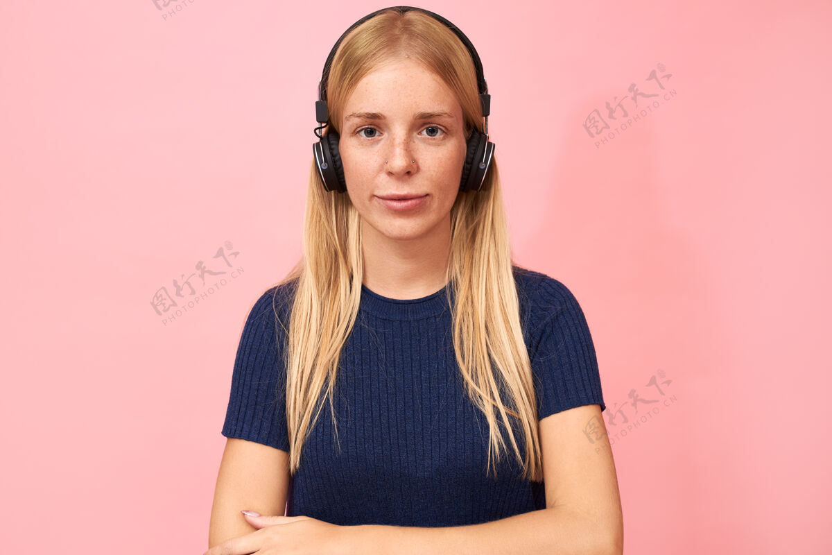 休闲时尚女学生的肖像 戴着粉色的鼻环 戴着无线耳机 听在线讲座 有声读物或播客时尚享受积极