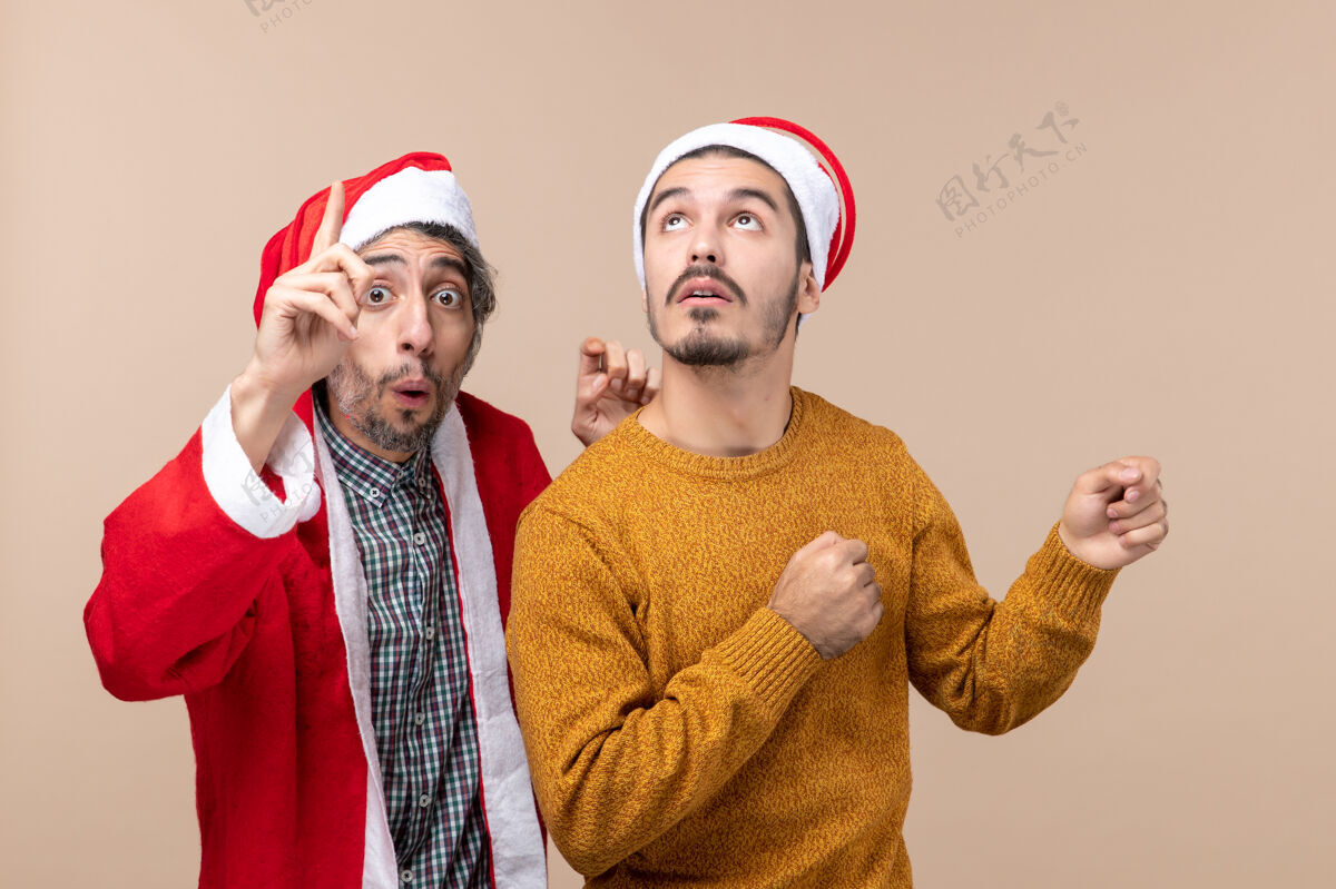 米色正面图两个戴着圣诞帽的朋友在高高的米色孤立的背景下看着帽子男性高