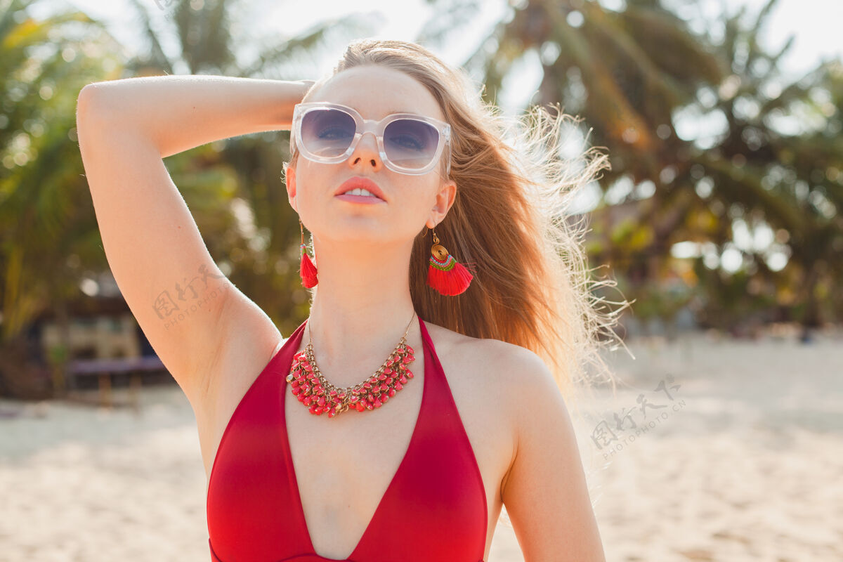 阳光年轻漂亮的金发女人穿着红色泳衣 戴着太阳镜在沙滩上晒太阳海滩性感胸部