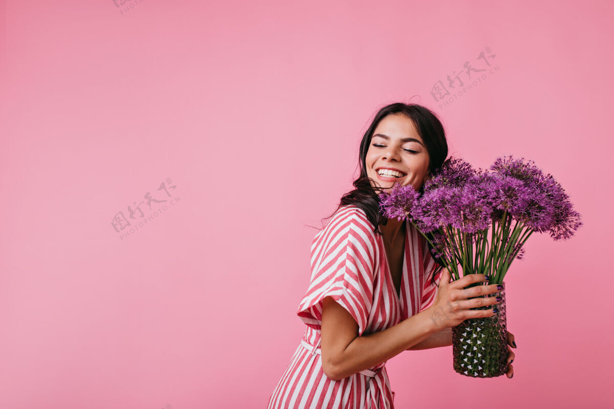 红色美丽的黑发女郎在欣赏送花的同时微笑得令人眼花缭乱身着粉色条纹上衣的女孩从幸福中闭上眼睛的画像阳光礼物自然