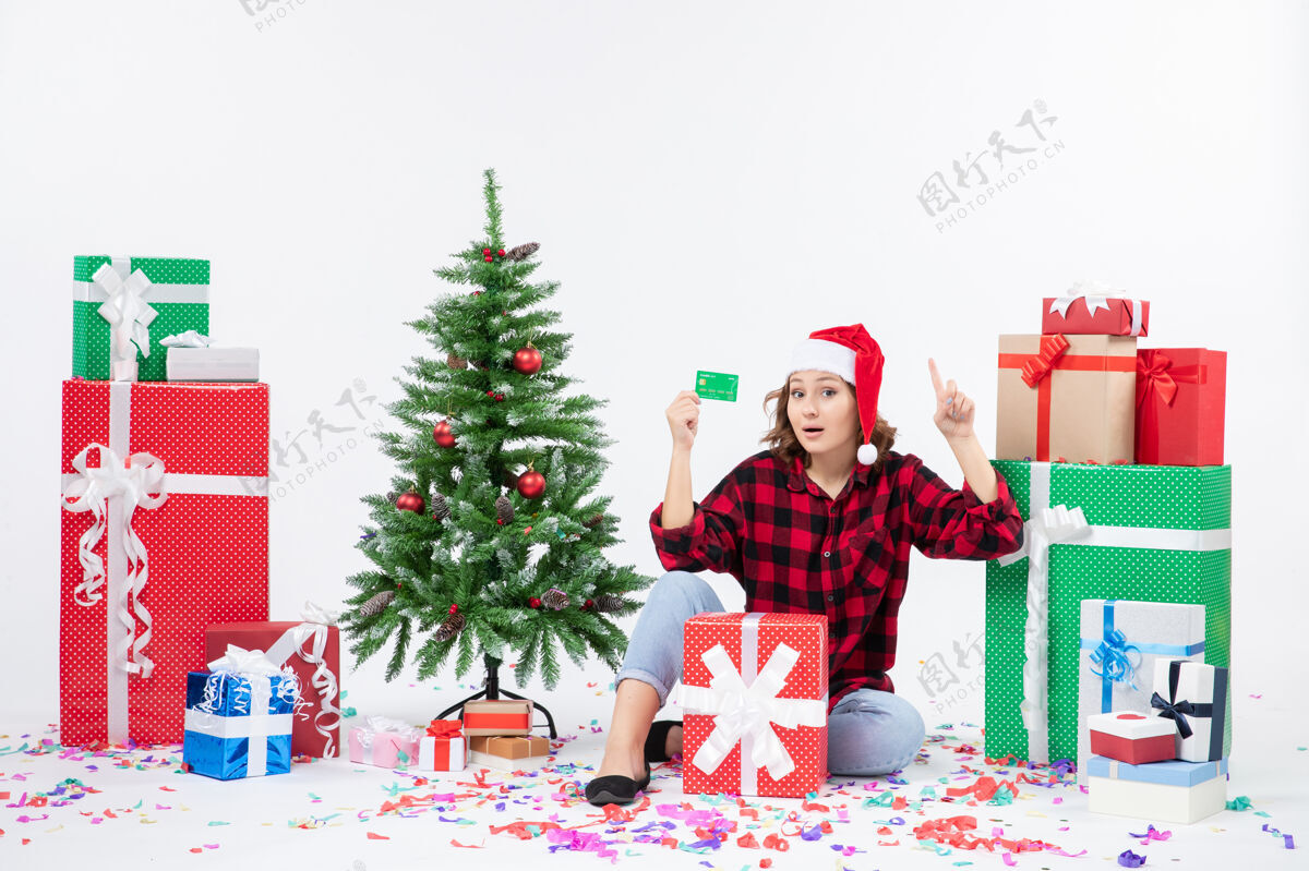 礼物正面图：年轻女子围坐在白墙上 手里拿着绿色的银行卡圣诞快乐前面坐着