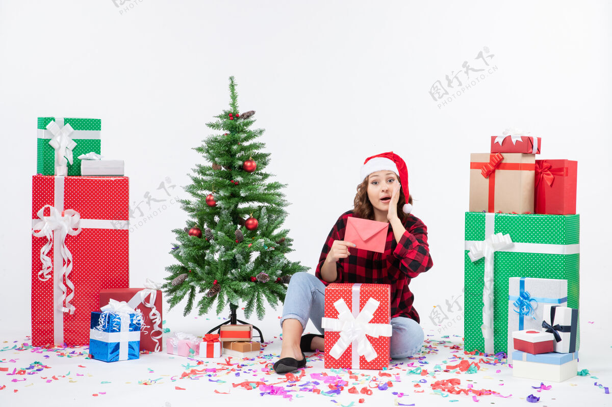 礼物前视图年轻女子坐在周围的礼物举行信封上的白墙拿着冬青圣诞快乐
