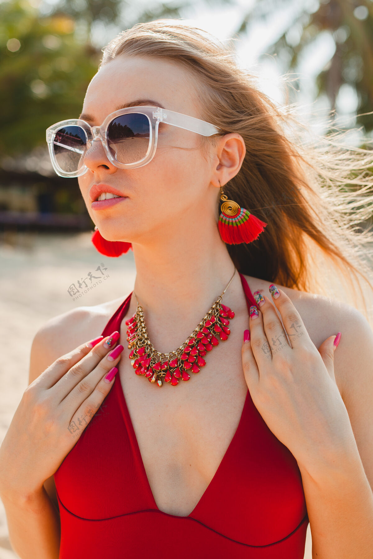 民族年轻漂亮的金发女人穿着红色泳衣 戴着太阳镜在沙滩上晒太阳身体项链性感