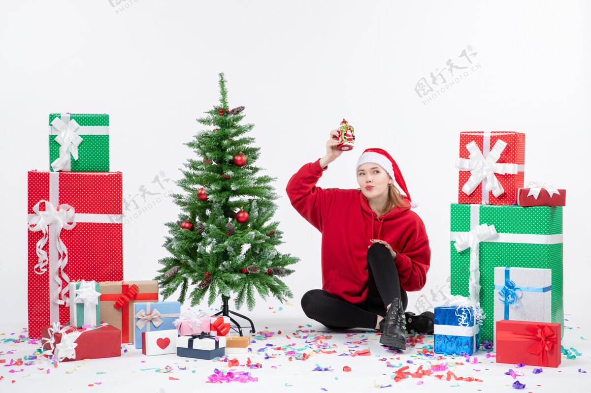 圣诞树前视图：年轻女子围坐在白色墙壁上拿着礼物抱着一些东西雪