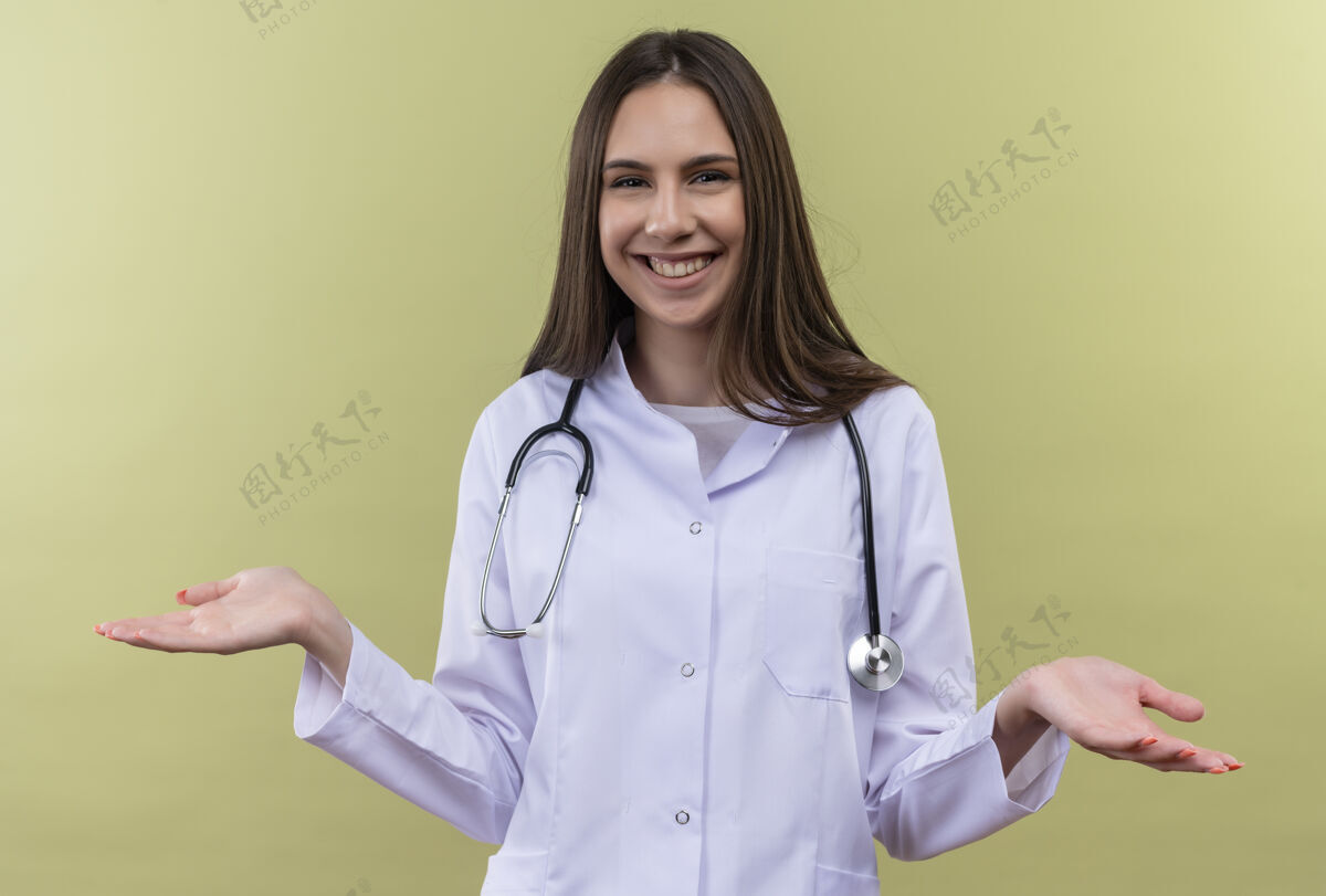 年轻带着微笑的年轻医生女孩穿着听诊器医用长袍在绿色背景上展开双手女孩长袍穿着