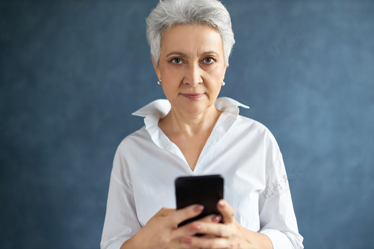 女性一位成功的中年女性高管的肖像 一头灰白的短发在手机上打短信应用程序互联网女商人