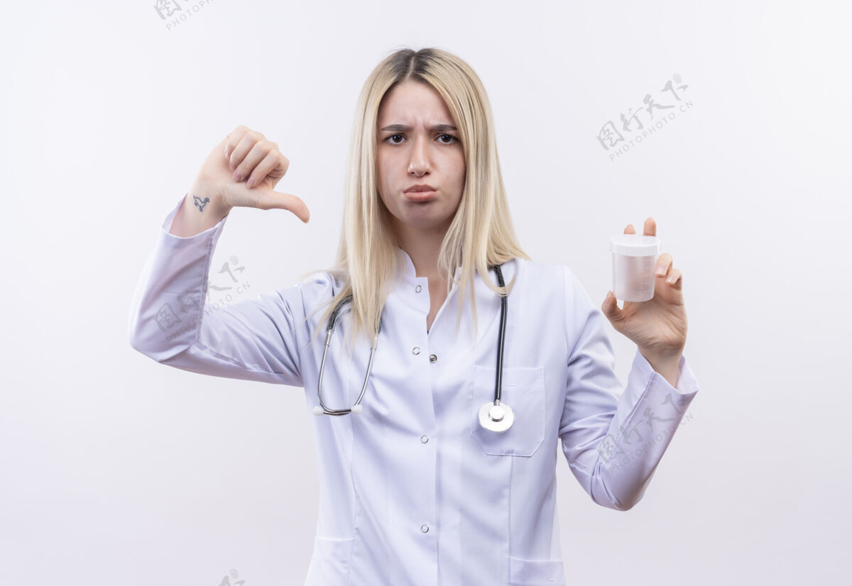 金发悲伤的医生 年轻的金发女孩 戴着听诊器 穿着医用长袍 空着大拇指 站在白色的背景上按住白色向下
