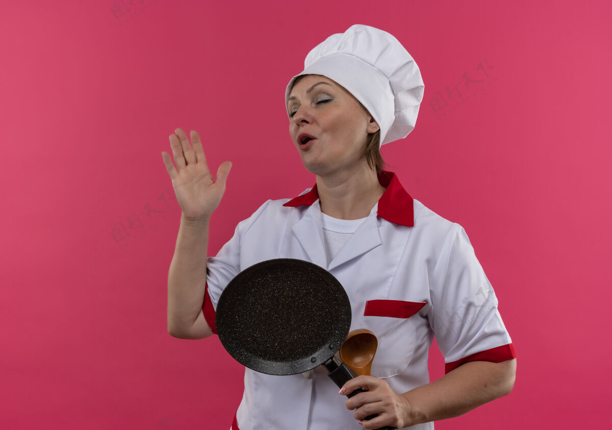 唱歌闭着眼睛 身着厨师制服的中年女厨师拿着煎锅唱歌女拿着煎炸