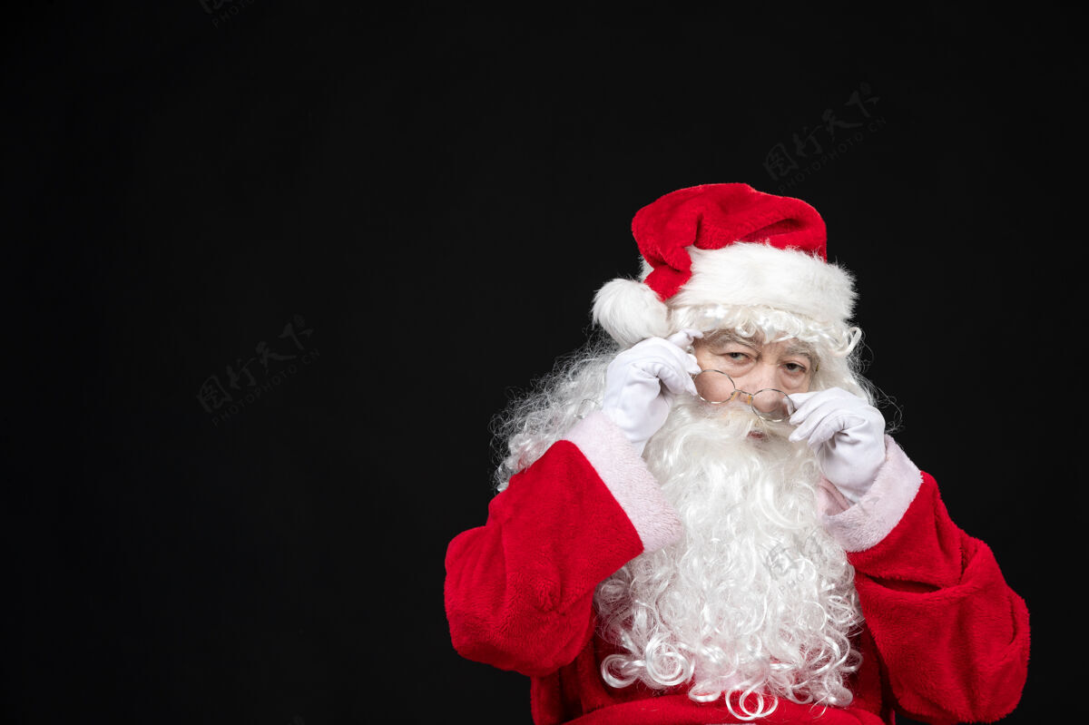 快乐圣诞老人穿着经典的红色套装 留着白胡子 站在黑色的墙上快乐人前面