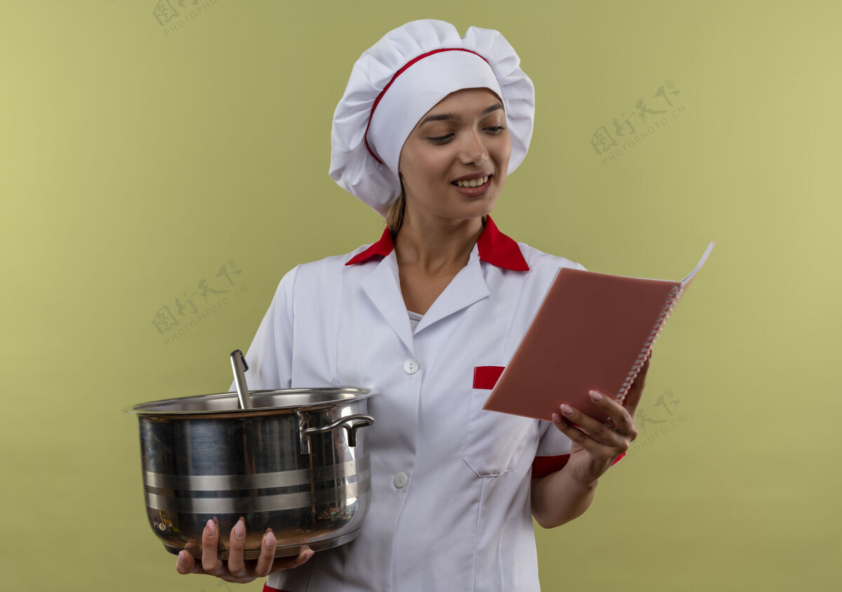 厨师年轻的女厨师面带微笑 身穿厨师制服 手里拿着平底锅 看着笔记本厨师拿着手