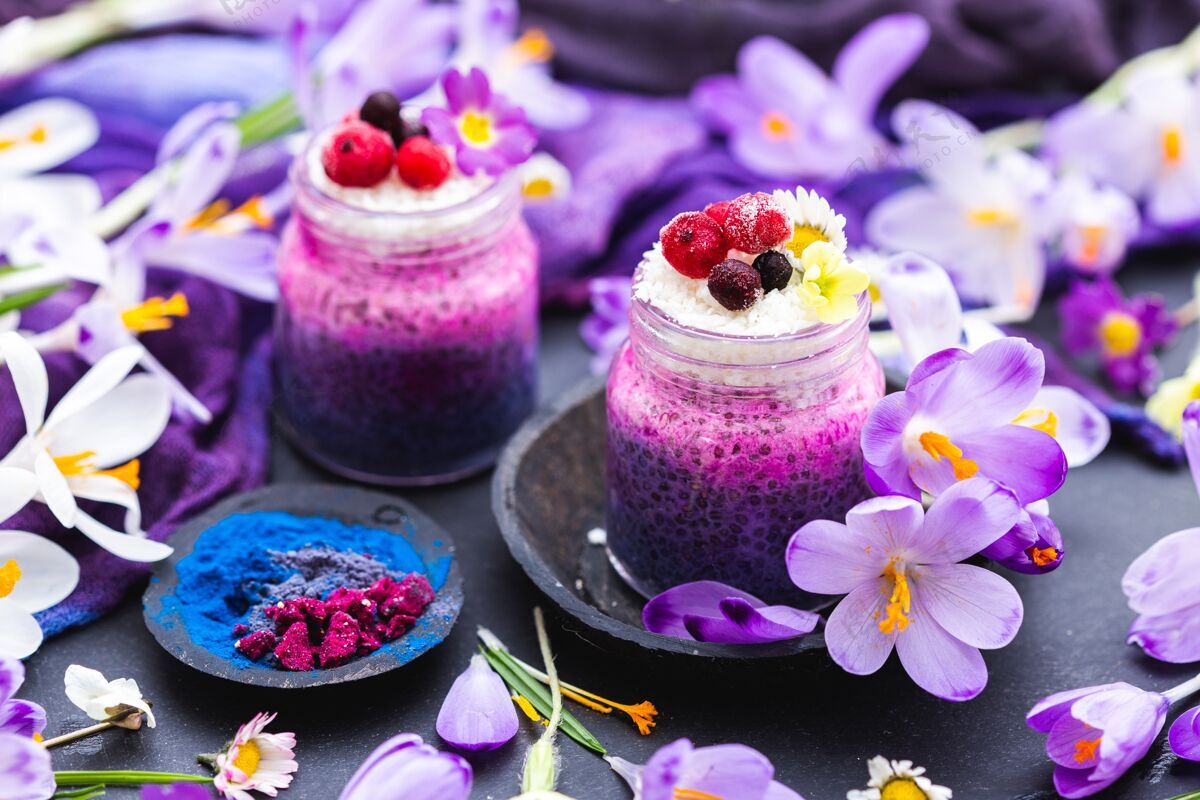 餐桌美丽的紫色春季素食冰沙展示装饰着五颜六色的花朵甜点蔬菜饮料