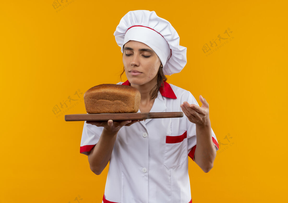 切着年轻的女厨师闭着眼睛 穿着厨师制服 拿着面包 嗅着面包放在有复印空间的砧板上面包女拿着
