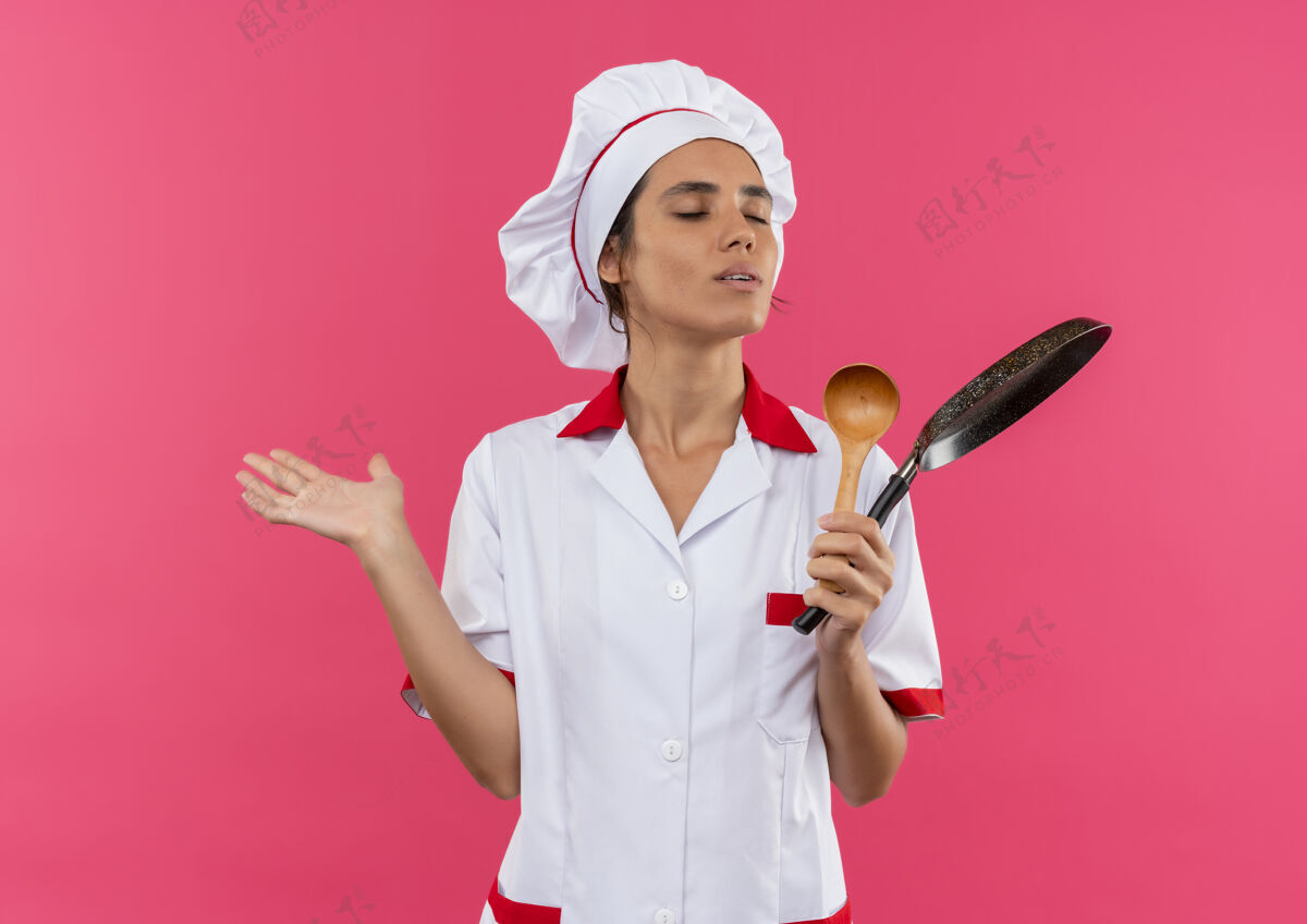 持有年轻的女厨师闭着眼睛 穿着厨师制服 手里拿着煎锅和勺子 还有复印空间封闭女平底锅