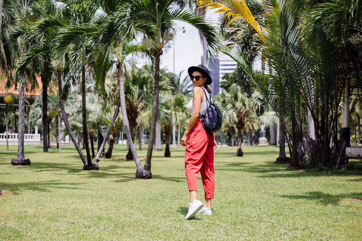 坐快乐女人背着背包环游曼谷 在绿草如茵的热带公园里享受美丽的晴天休闲休息优雅