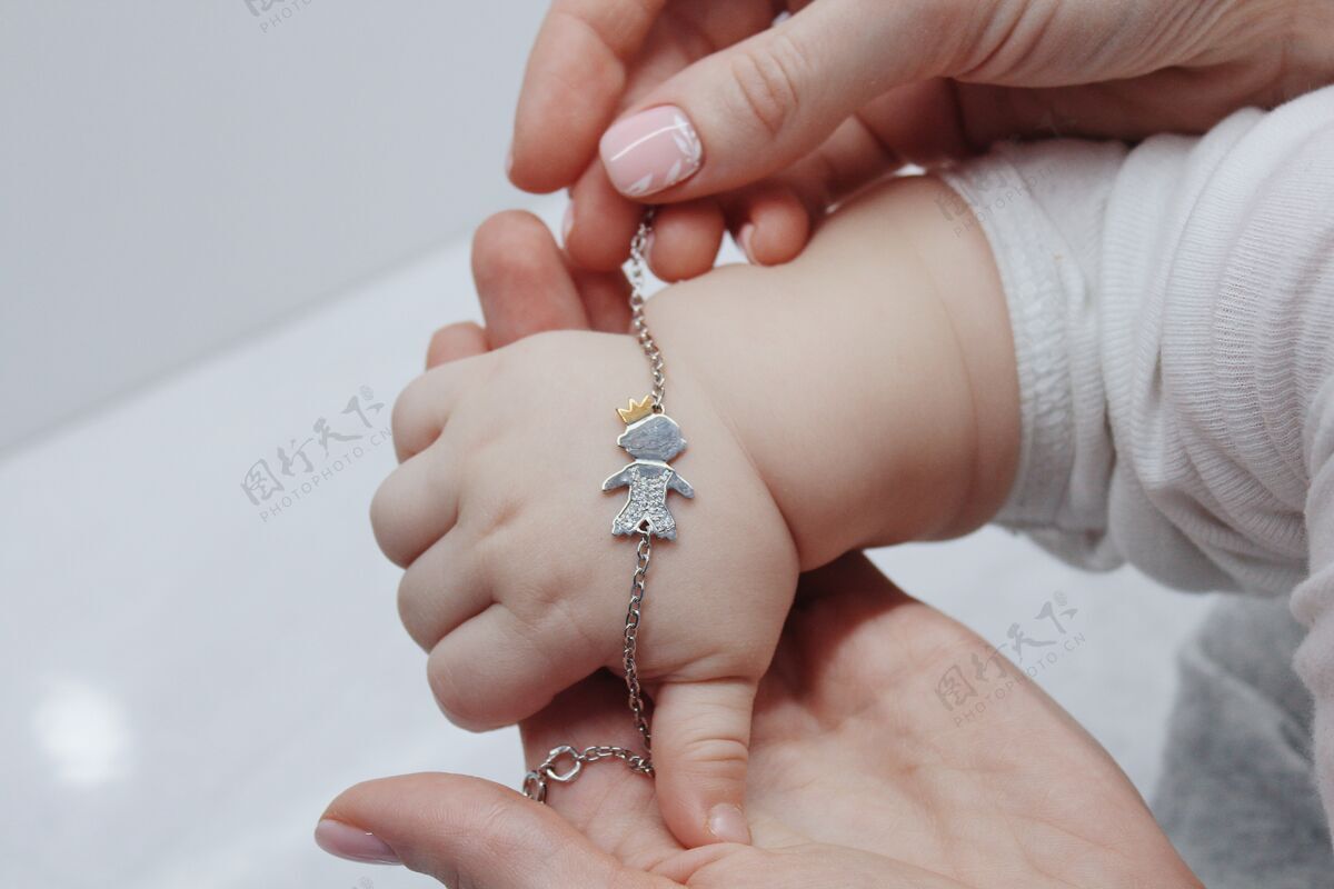 人类特写镜头一个女人把一个可爱的手镯放在她的宝宝的手上头发手镯孩子