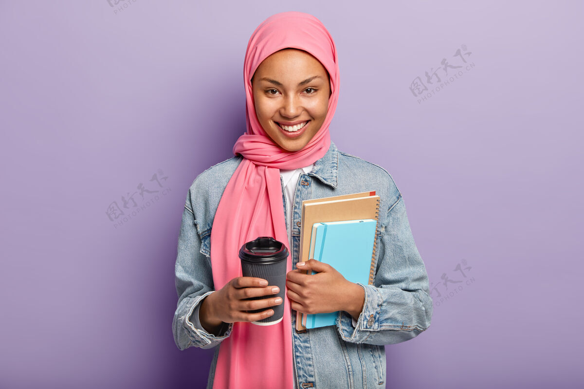 乐观开朗的妇女戴着粉色头巾 穿着牛仔外套 拎着钱包日记高兴正面