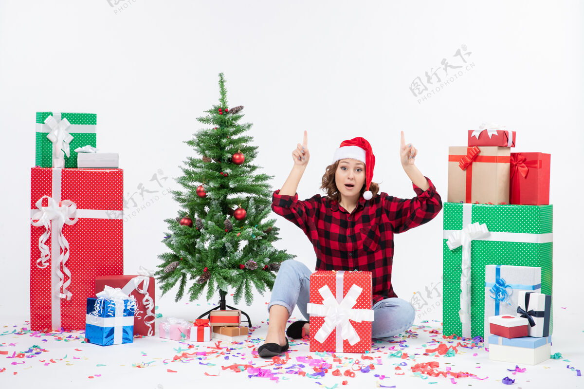 装饰年轻女子围坐在礼物和白色墙上的小圣诞树前的视图雪礼物冬青