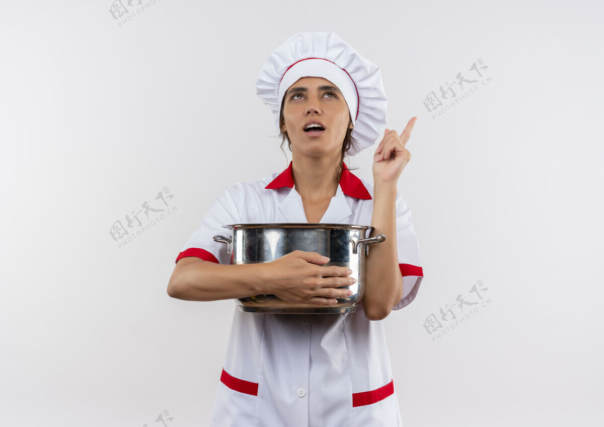 思考看着一个年轻的女厨师 穿着厨师制服 拿着平底锅 指着隔离的白色墙壁 上面有一个复制空间厨师制服分