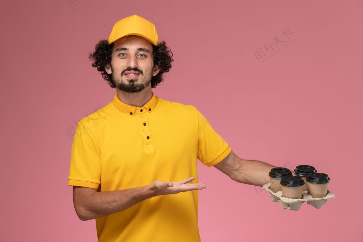 人正面图穿着黄色制服的男信使拿着棕色的咖啡杯在粉红色的墙上快递人棕色