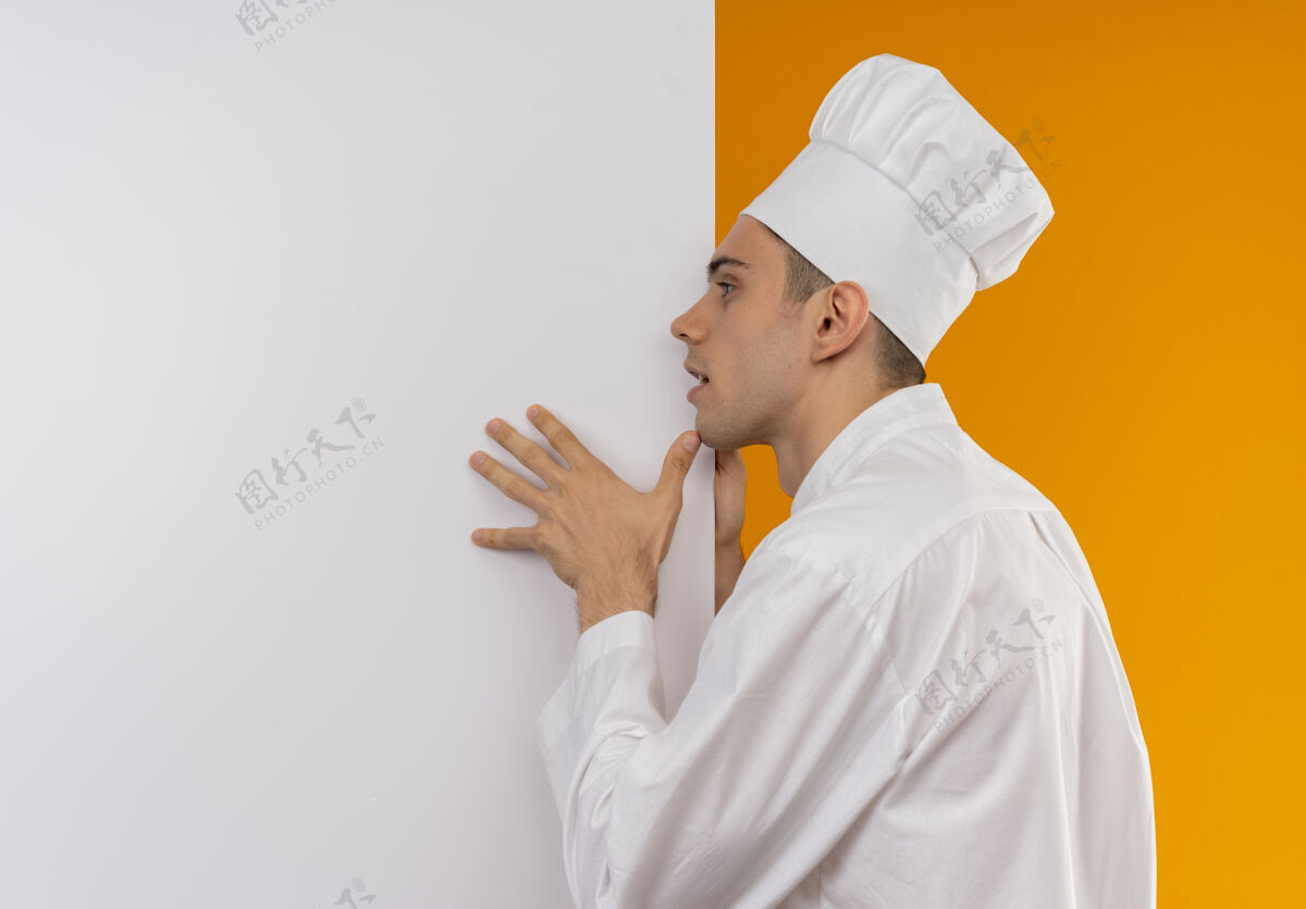 侧看着旁边年轻的男酷穿着厨师制服拿着白色的墙 隔离着黄色的墙和临摹的空间厨师制服抱