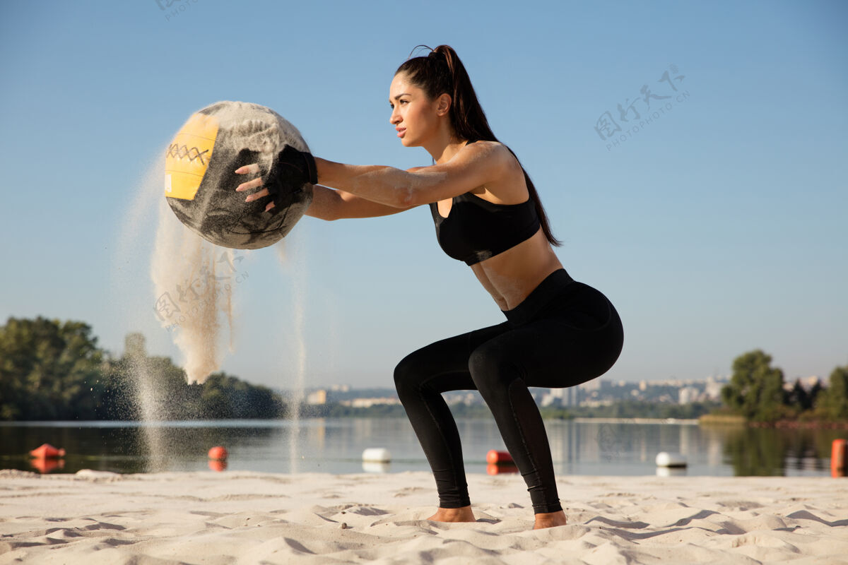 年轻年轻健康的女人在沙滩上拿着球蹲着健康锻炼肌肉