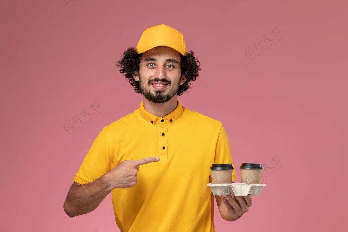 男快递员正面图：身穿黄色制服 披风的男性快递员在粉色墙上拿着送货咖啡杯人工人正面