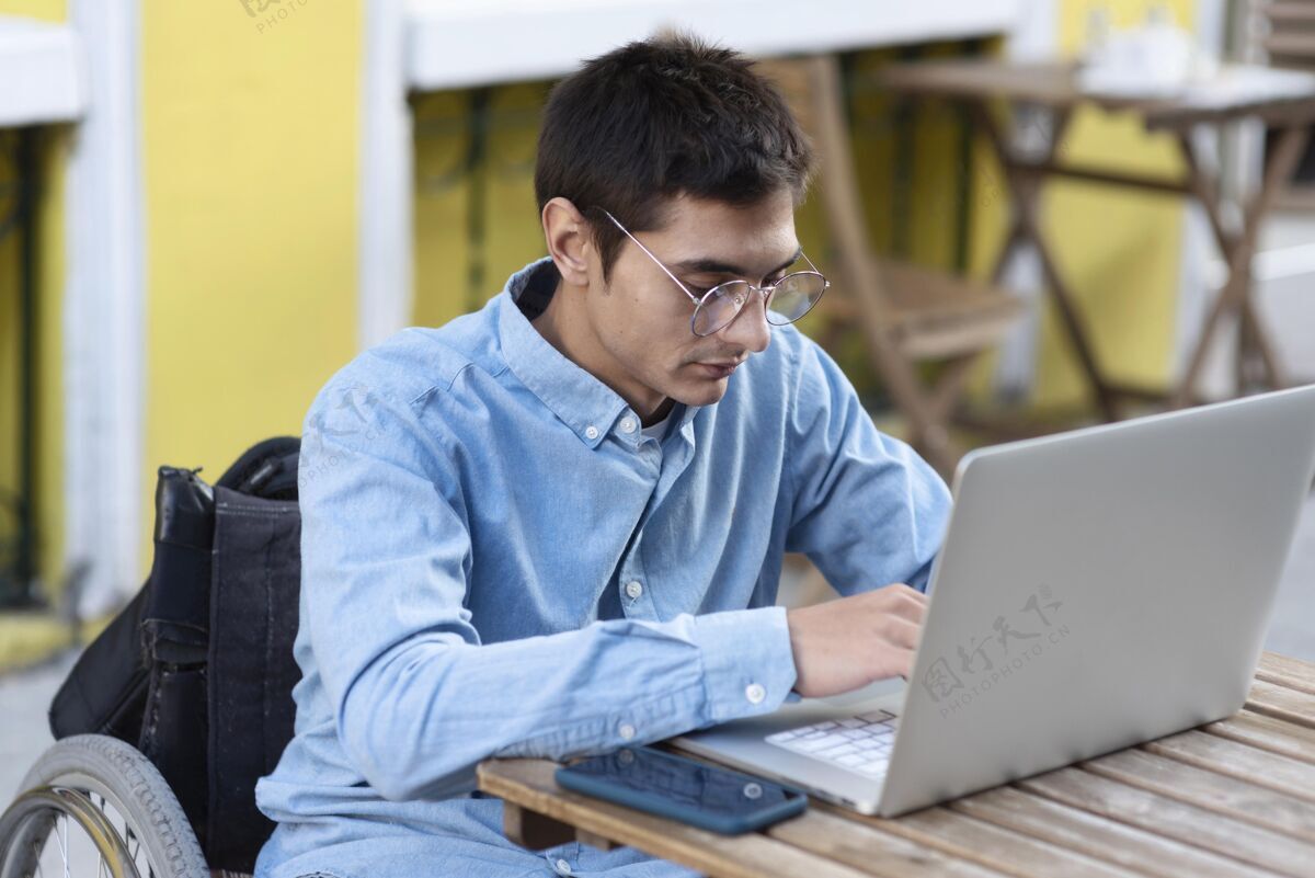 笔记本电脑坐在轮椅上用笔记本电脑工作的人水平户外残疾人