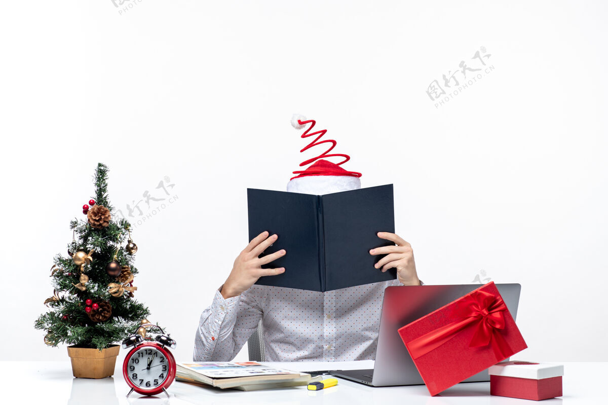 商人忙碌的年轻商人戴着滑稽的圣诞老人帽子在白色背景的办公室里查看文件中的信息信息惊喜包装