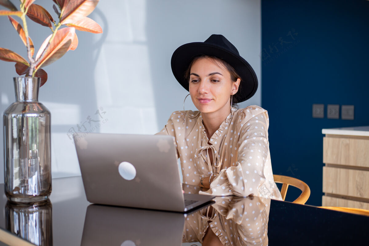 坐姿穿着正装戴着经典帽子的欧洲女人在家里厨房工作企业家网络家庭