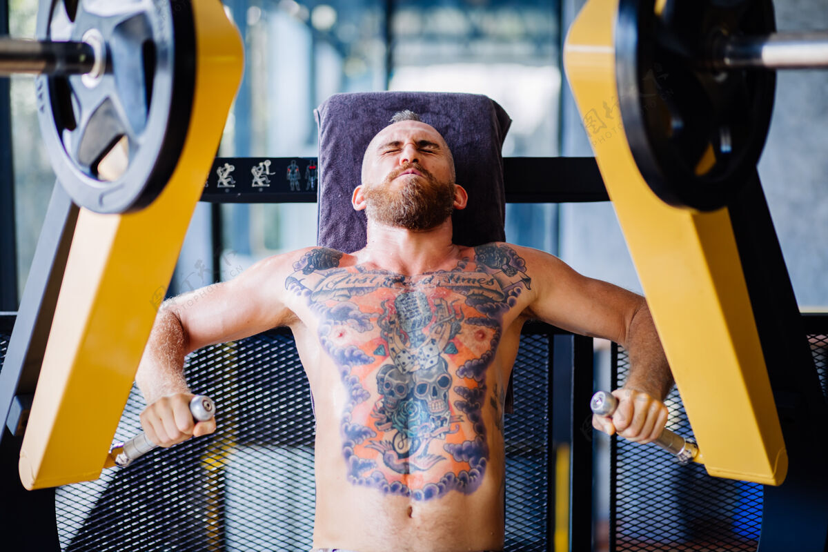 重在靠近窗户的健身房里 纹身的大胡子男人在胸部按压机上锻炼的肖像健康性感运动员
