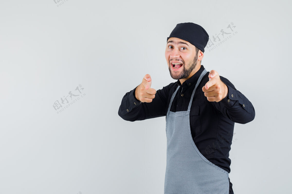 手势男厨师穿着衬衫 围裙上显示出持枪的姿势 指着镜头 看上去很开心 前视图看厨师人