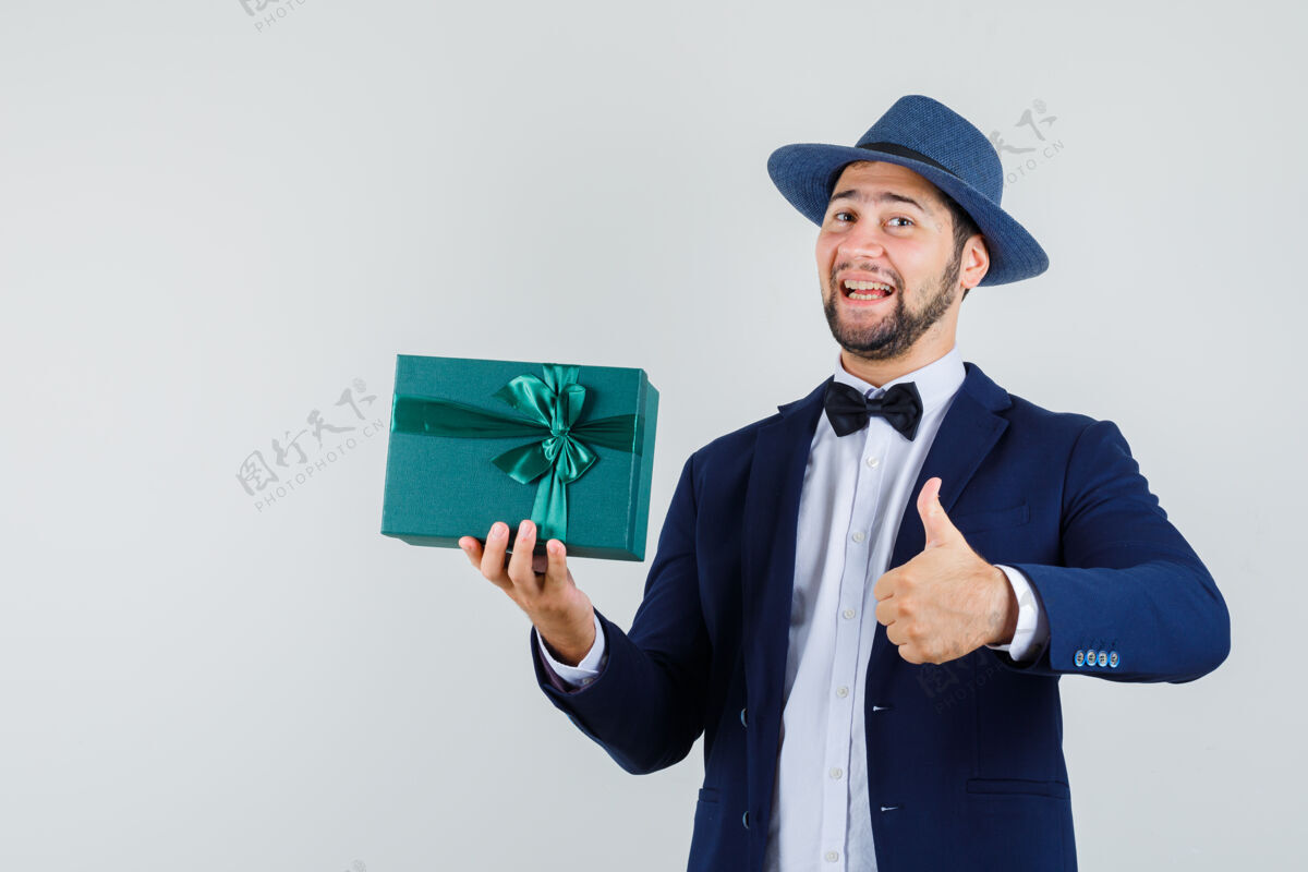 向上年轻人拿着礼物盒 大拇指朝上 穿着西装 戴着帽子 看上去很高兴男人年轻帅气