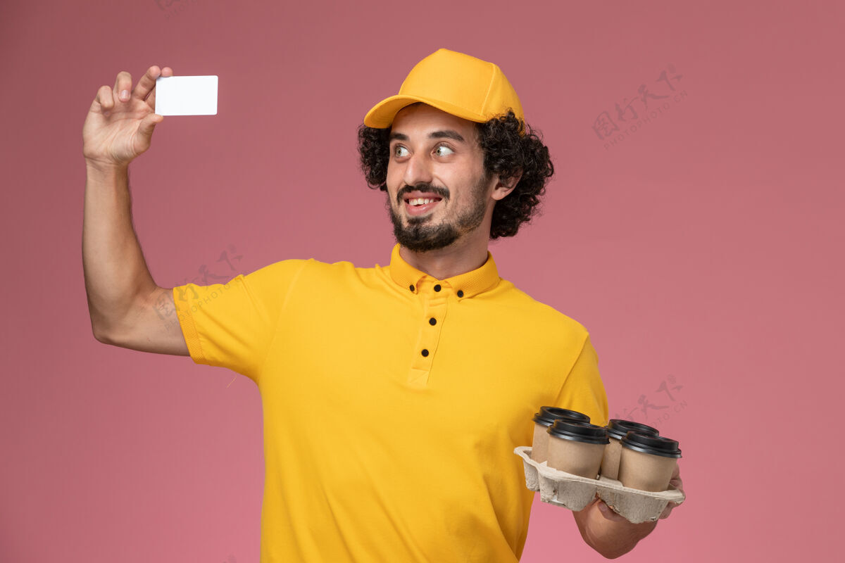 制服正面图：身穿黄色制服的男信使手拿棕色咖啡杯 粉色墙上挂着白色卡片男性棕色服务