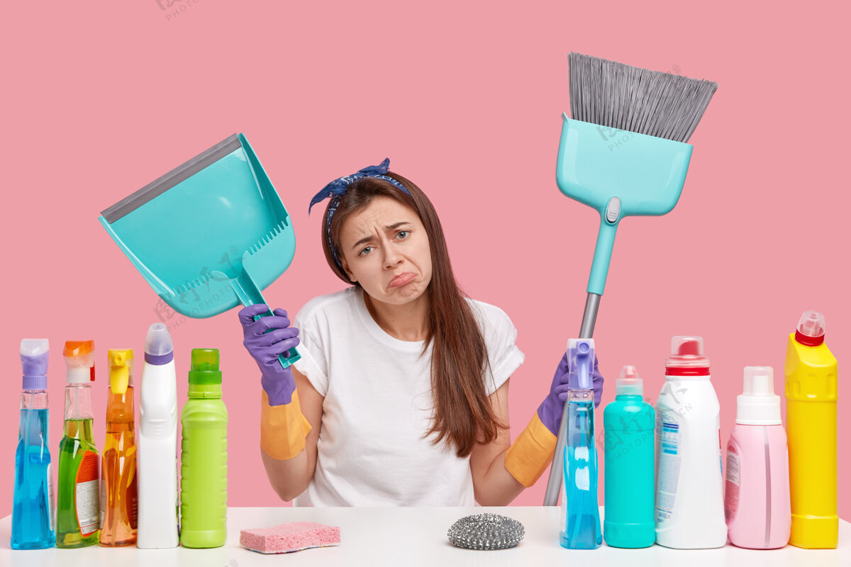 墙沮丧沮丧的年轻女佣不满地皱起眉头 拿着勺子和扫帚 打扫卫生卫生海绵不满