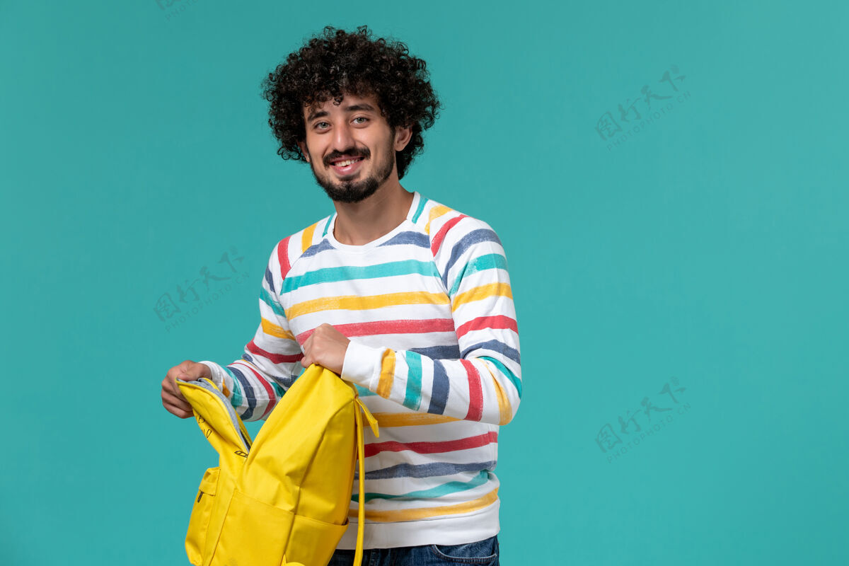 快乐男学生拿着黄色背包和文案在蓝色墙上微笑的正面图大学正面举行