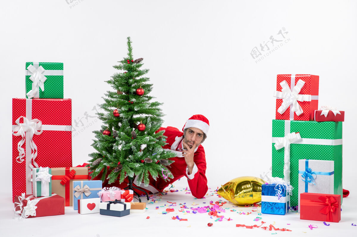 圣诞圣诞心情与年轻的圣诞老人躲在圣诞树附近的礼物在不同颜色的白色背景图片不同圣诞老人季节性
