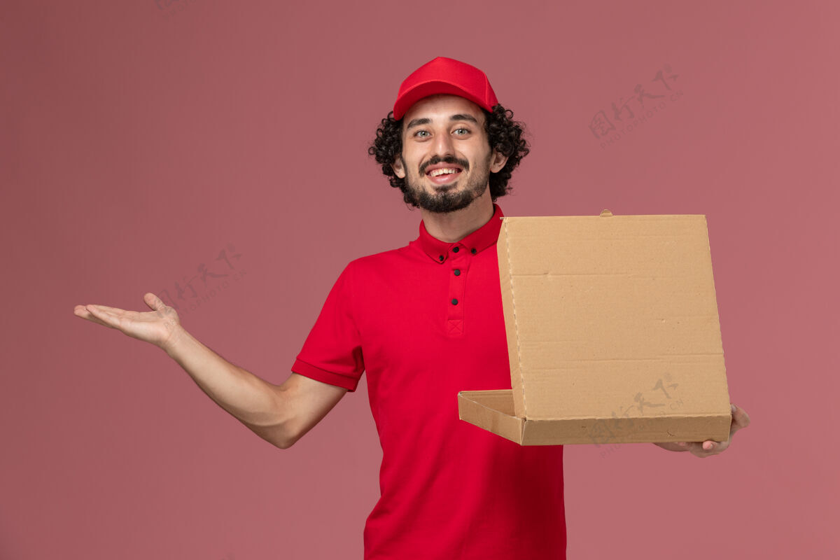 员工正面图穿着红色衬衫和披风的男信使拿着粉红色墙上的食品盒帽子人微笑