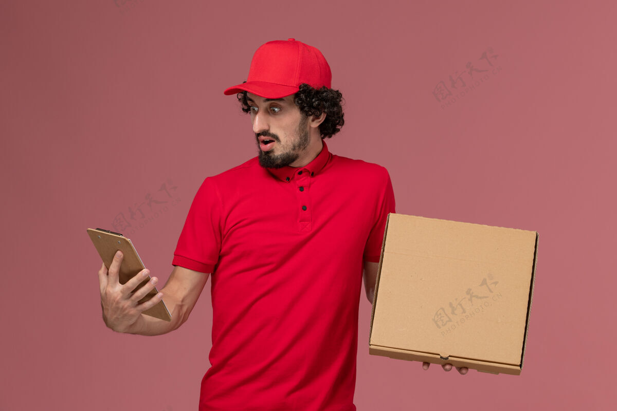 粉色正面图：身穿红色衬衫和披风的男性快递员在粉色墙上拿着快递食品盒和记事本男成人人