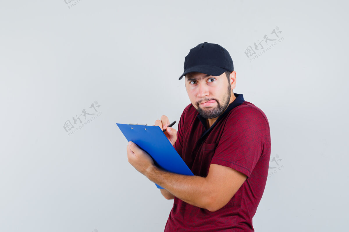 写作穿着红色t恤 戴着黑色帽子的年轻男子一边向前看 一边在笔记本上写着什么 一边看着前方的景色严肃男人传递